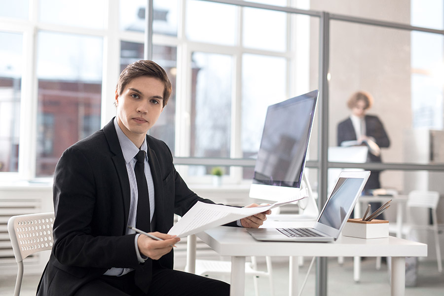 Serious and confident businessman with papers looking at camera by workplace while looking through new contracts